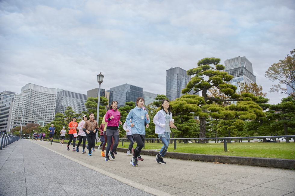 a group of people running on a sidewalk in front of a city