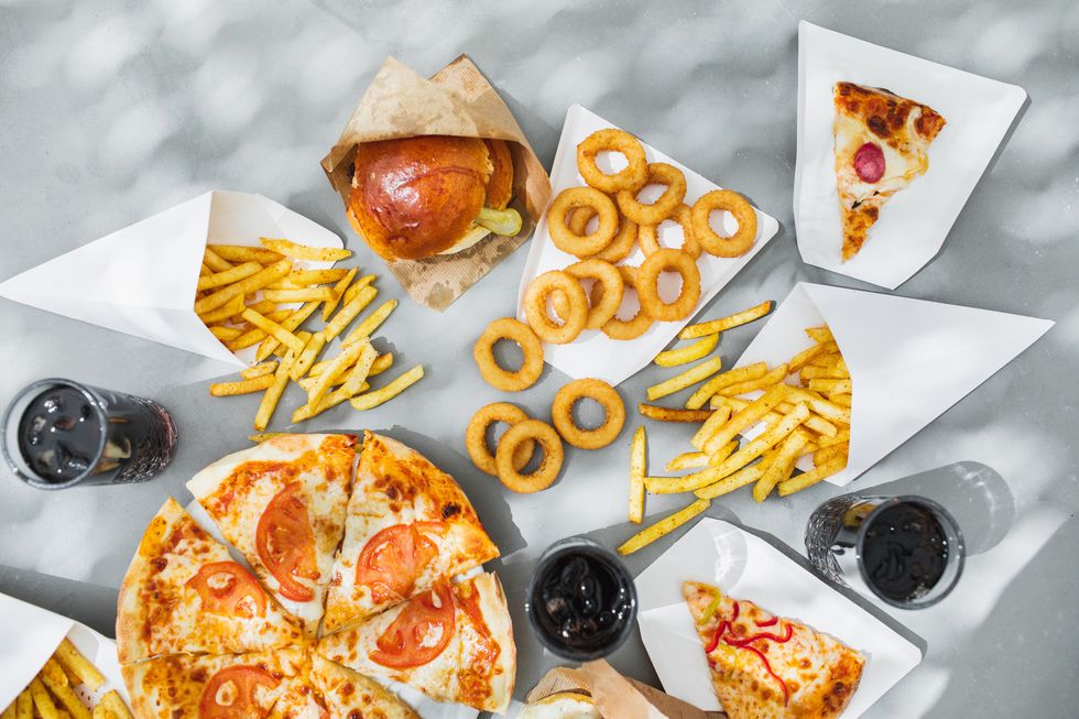 assorted take out food such as pizza, french fries, onion rings, burger and cola