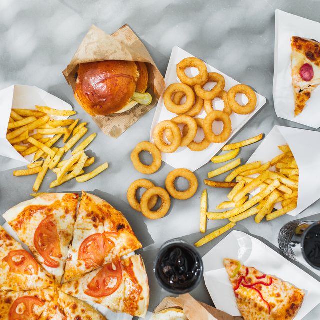 assorted take out food such as pizza, french fries, onion rings, burger and cola.