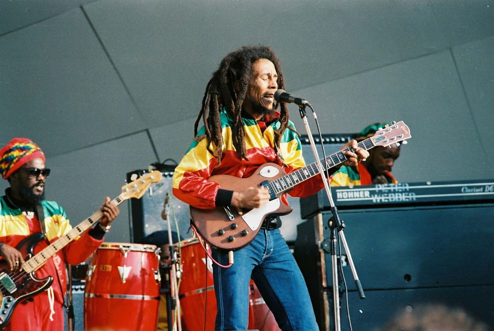 bob marley holding a guitar and singing as he stands in front of a microphone