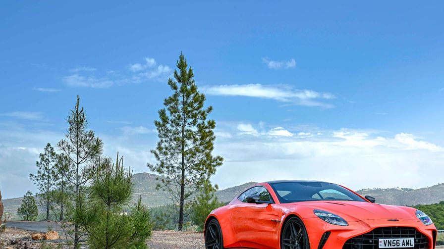 a red sports car parked on a road with trees and mountains in the background