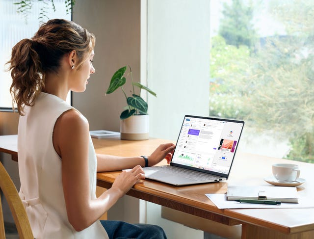 person working on a laptop at a table with plants and a cup