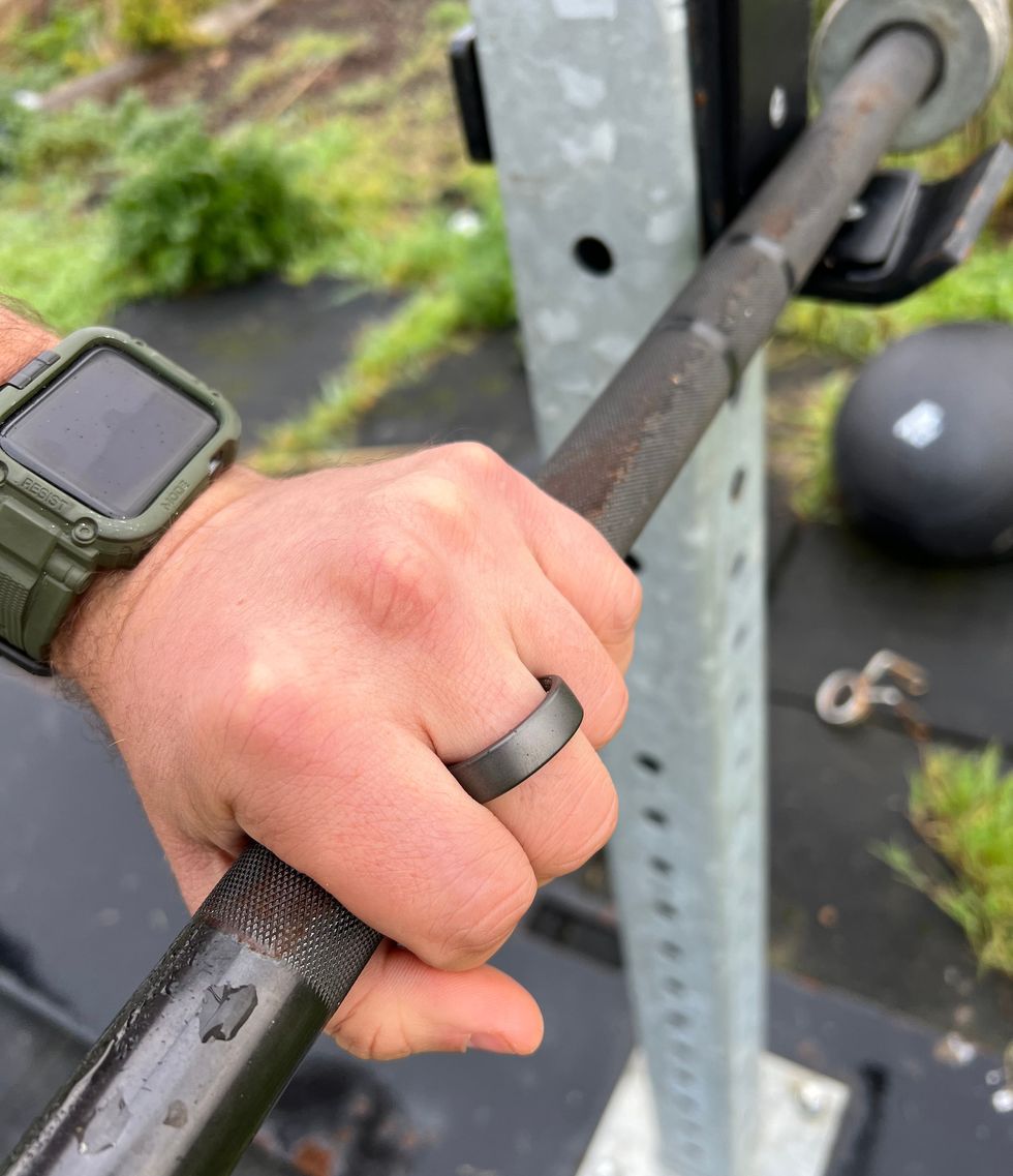 a hand wearing an oura smart ring holding a barbell
