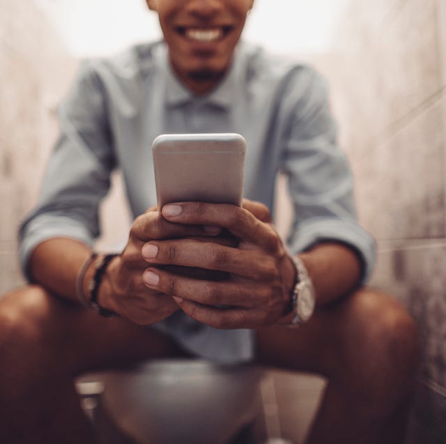 man looking at his phone while on the toilet