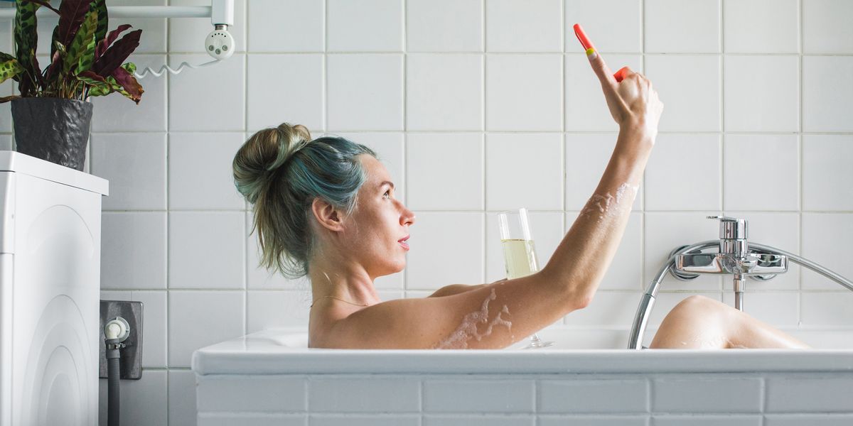 woman in bathtub taking a selfie with champagne