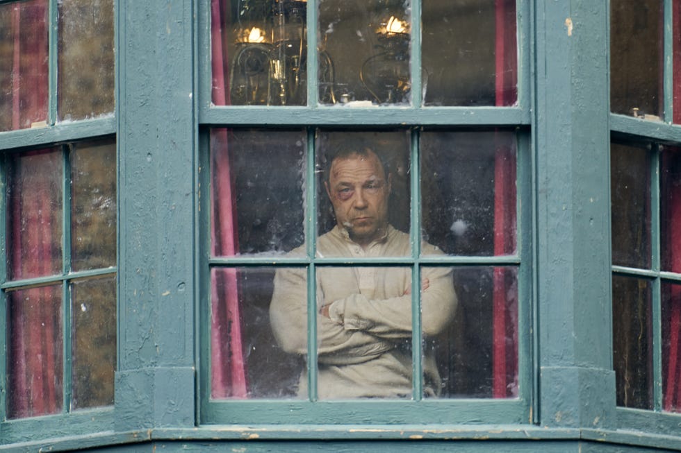 Person standing behind a large window with wooden frames