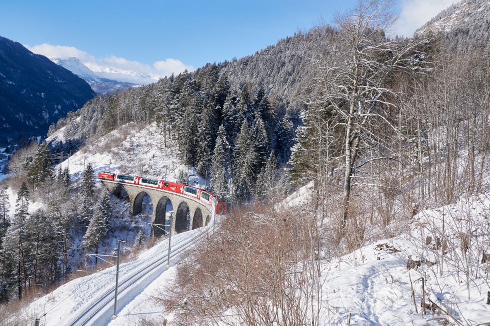 scenic view of a train crossing a snowy viaduct surrounded by mountains and forests