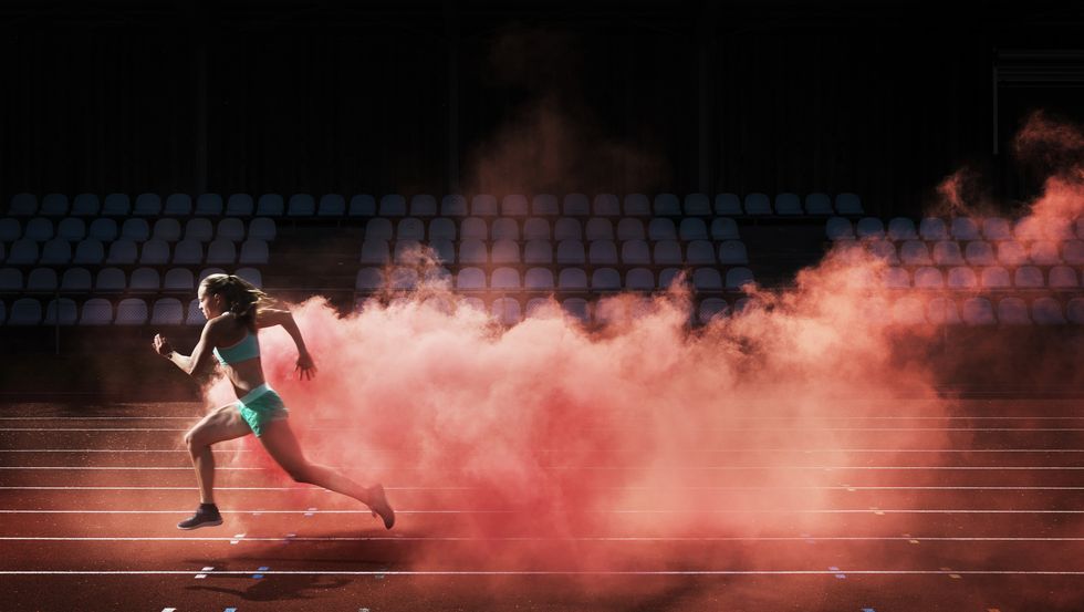 ragazza che corre con fumo dietro rosso in una pista di atletica