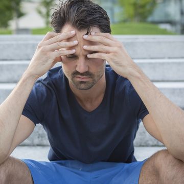 athlete sitting on stairs with hands on head, having a headache