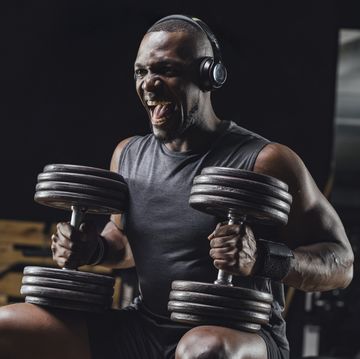 Donkere man laat zich motiveren door muziek om met dumbells te sporten in de gym
