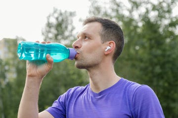 athlete with wireless in ear headphones using a reusable plastic bottle for drinking during a workout in the park