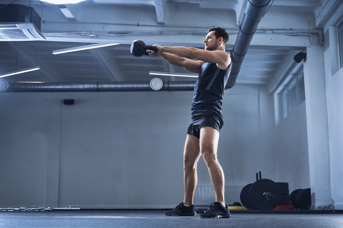 Athletic man doing kettlebell swing exercise at gym