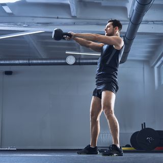 athletic man doing kettlebell swing exercise at gym