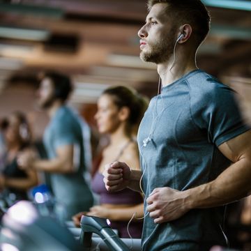 athletic man listening music while running on treadmill in a gym.