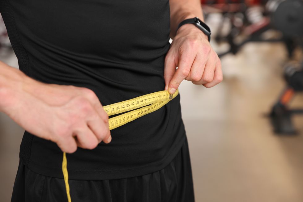 athletic man measuring waist with tape in gym, closeup