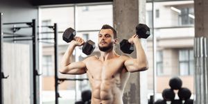 athletic man with a naked torso trains his shoulders with dumbbells in his hands workout in the gym bodybuilding and fitness, healthy lifestyle