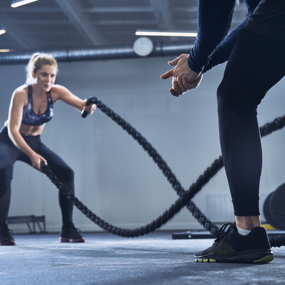 Athletic woman doing battlerope exercise with personal trainer at gym
