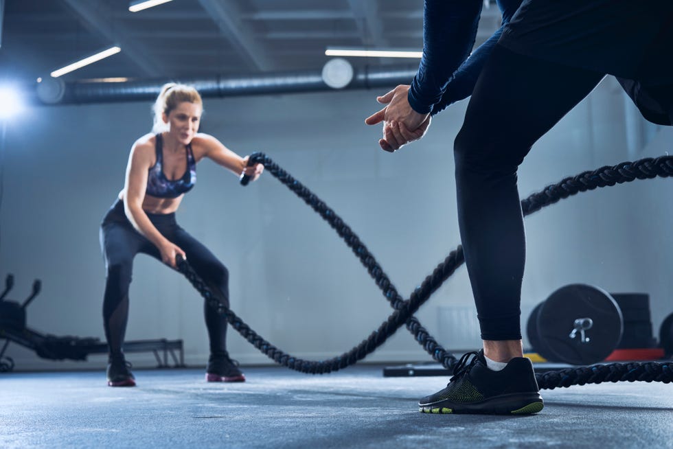 Athletic woman doing battlerope exercise with personal trainer at gym