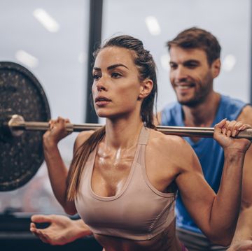 athletic woman having weight training with her coach in a gym