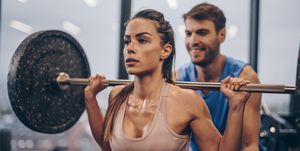 athletic woman having weight training with her coach in a gym