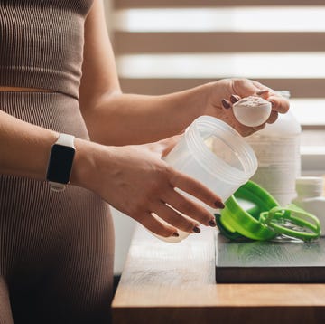 Athletic woman in sportswear with measuring spoon in her hand puts portion of whey protein powder into a shaker on wooden table with amino acid white capsules, bananas and apple, making protein drink athletic woman in sportswear with measuring spoon in her hand puts portion of whey protein powder into a shaker on wooden table with amino acid white capsules, bananas and apple, making protein drink
