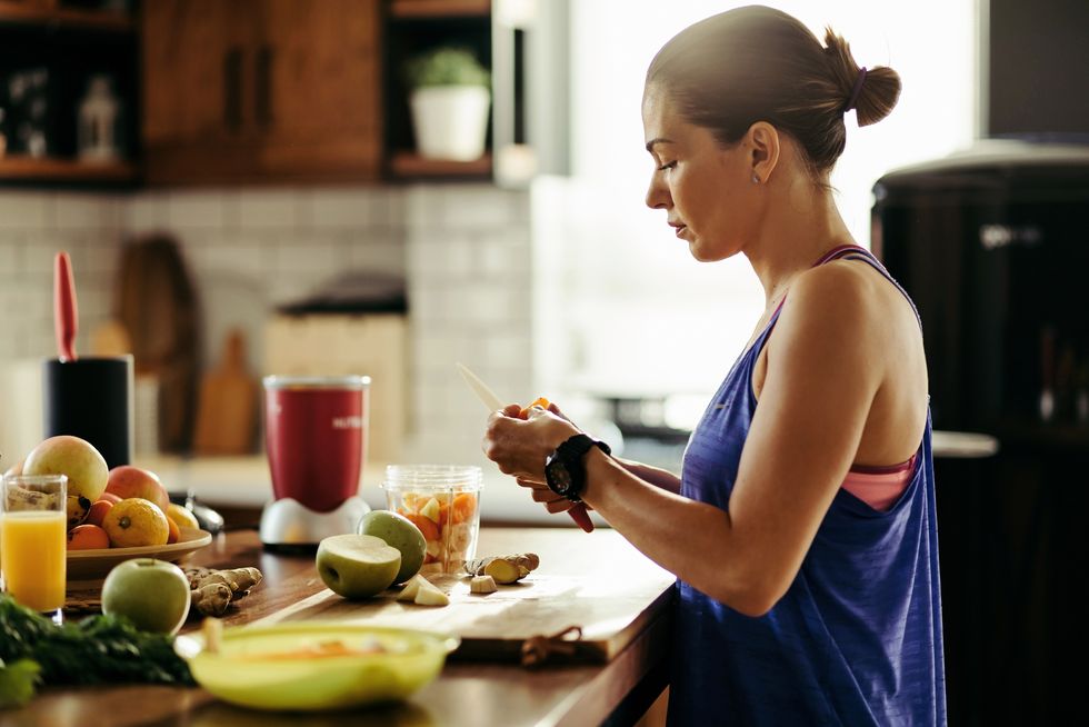 athletic woman slicing fruit while preparing smoothie in the kitchen
