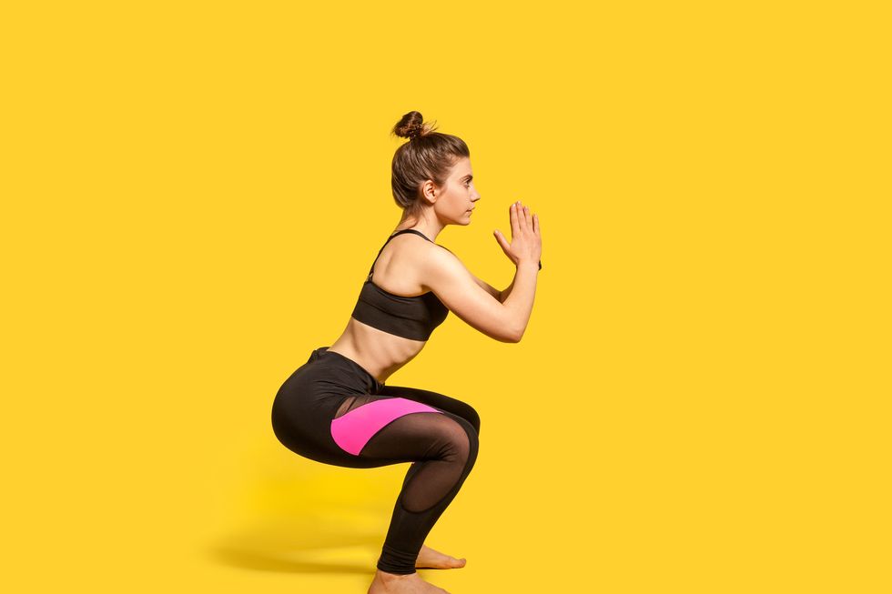 athletic woman with hair bun in tight sportswear doing squat, lower body sport exercise, keeping balance