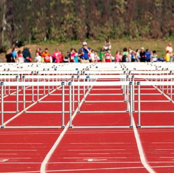 athletics hurdles placed on the tartan of the outdoor athletics track ready to start the race in the background a large number of athletes waiting to participate