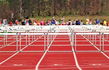 athletics hurdles placed on the tartan of the outdoor athletics track ready to start the race in the background a large number of athletes waiting to participate