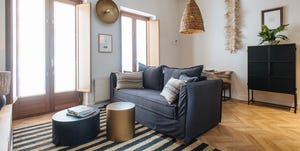 salón con sofá tapizado en negro, alfombra de rayas de fibras, mesas auxiliares de diseño circular en bloque y lámpara de techo de fibras