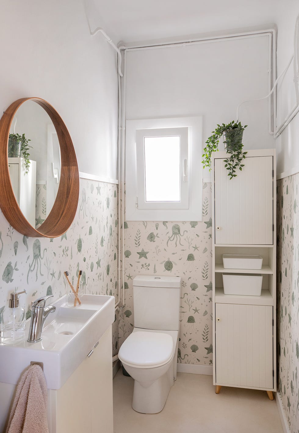 baño con muebles blancos y papel pintado con motivos marinos
