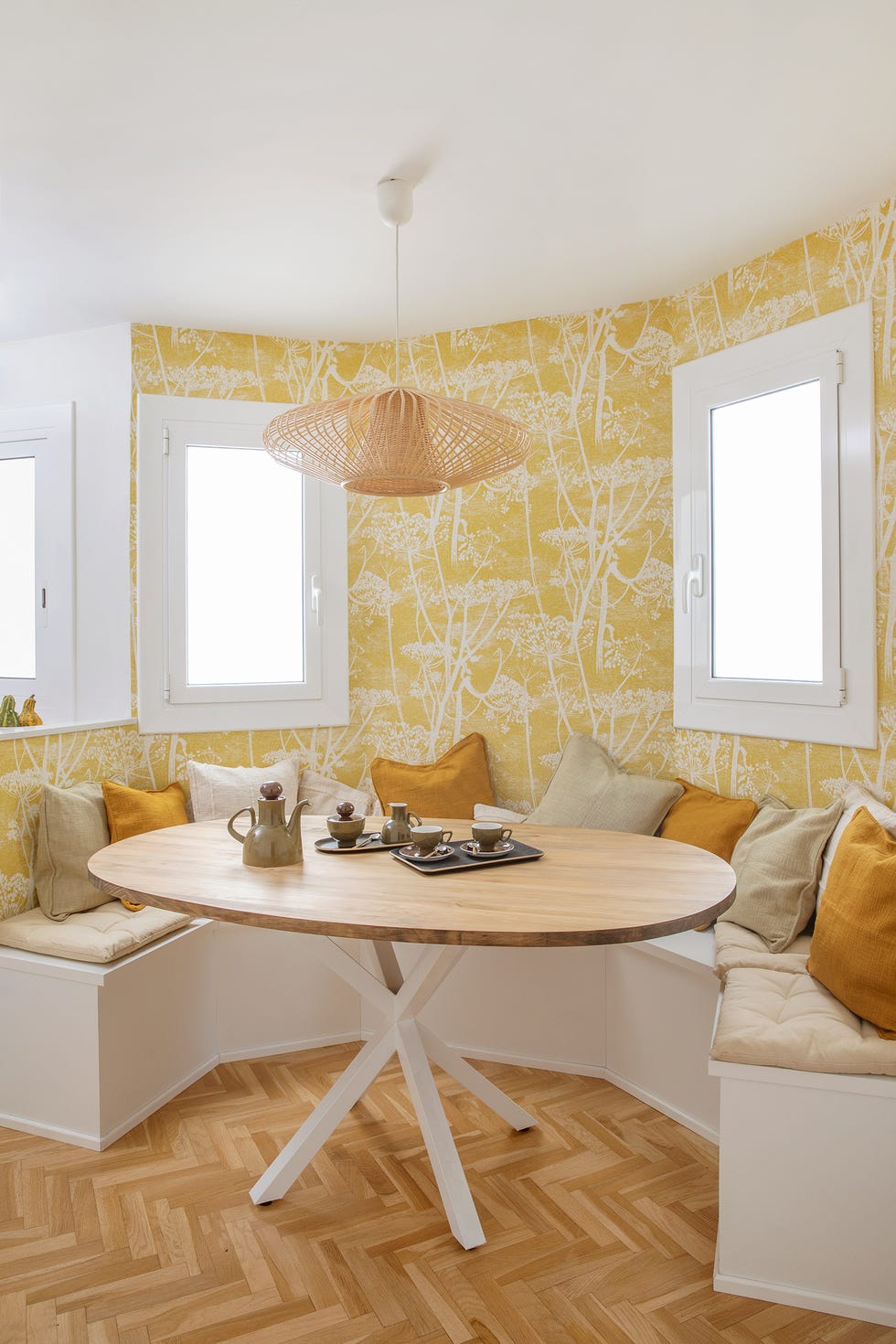 office con papel pintado amarillo con dibujos de árboles, banco en u y mesa de madera ovalada