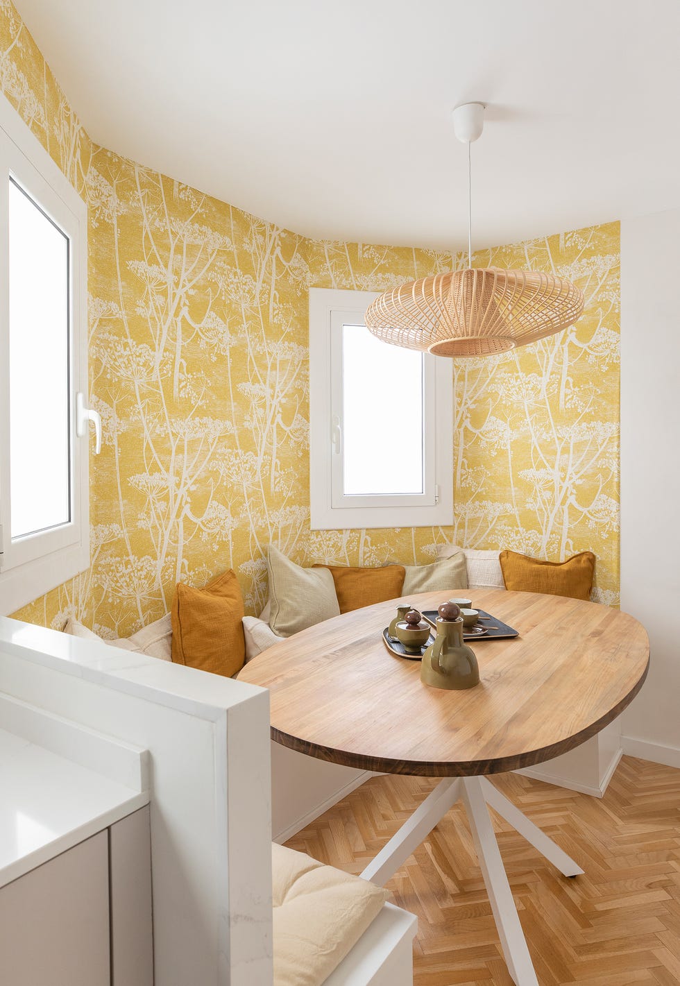 office con papel pintado amarillo con dibujos de árboles, banco en u y mesa de madera ovalada