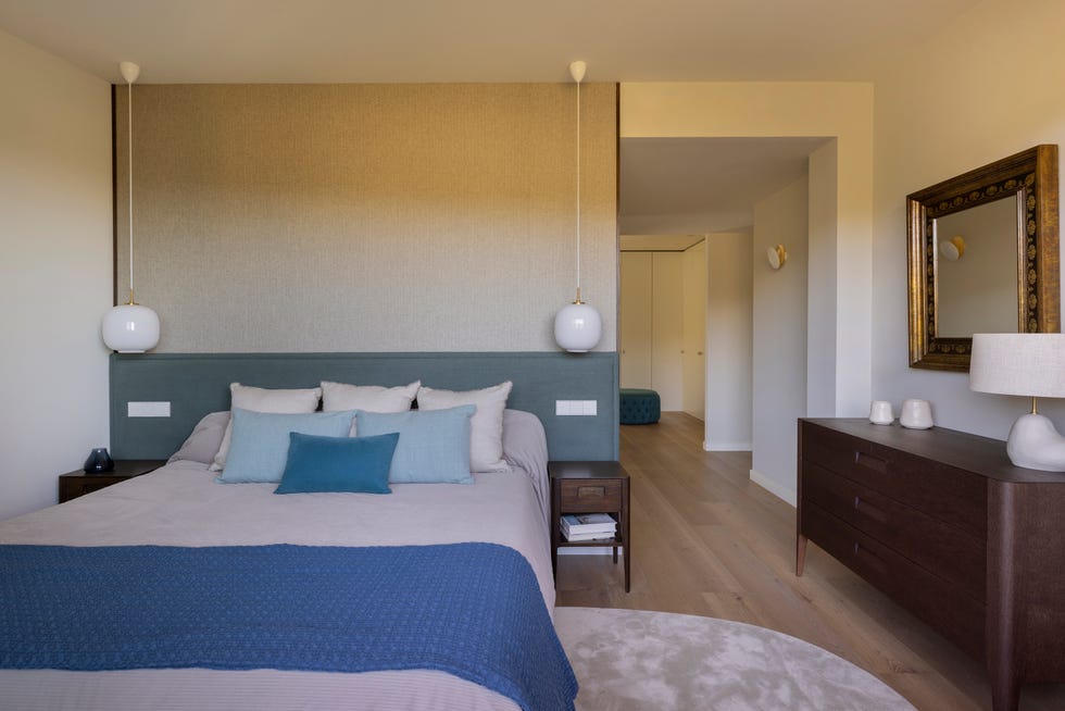 cama con cabecero azul, lámparas suspendidas y cómoda de madera