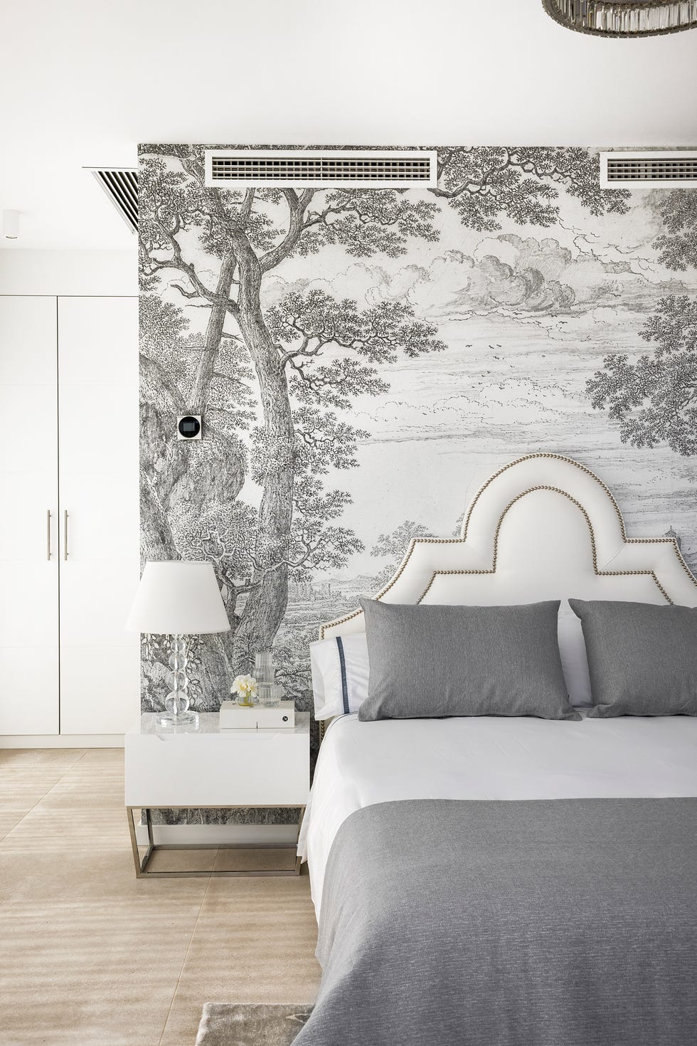 dormitorio con cabecero clásico acolchado en blanco con remaches dorados, mesita de diseño en blanco y papel pintado en tonos grises