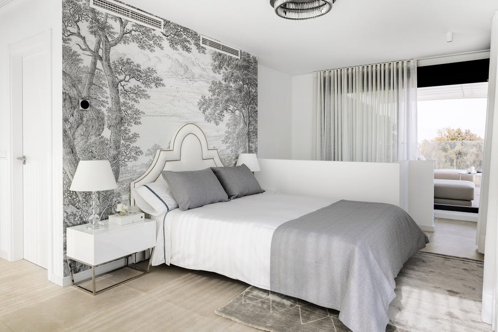 dormitorio con cabecero clásico acolchado en blanco con remaches dorados, mesita de diseño en blanco y papel pintado en tonos grises