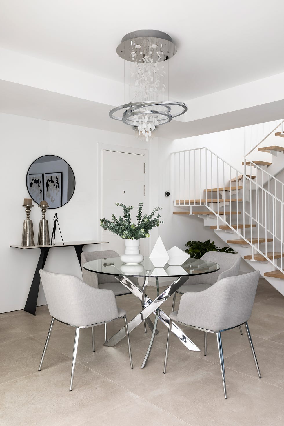 comedor moderno con mesa redonda con el sobre de cristal y las patas de acero y sillas tapizadas en gris