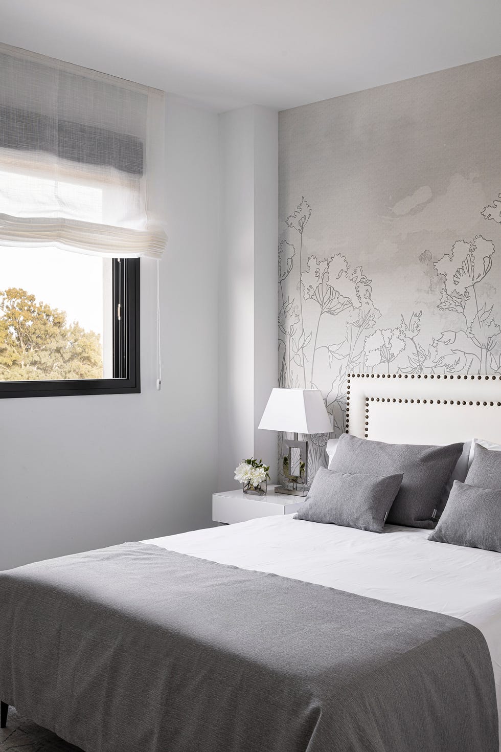 dormitorio con cabecero acolchado en blanco con remaches y papel pintado con motivos florales en gris