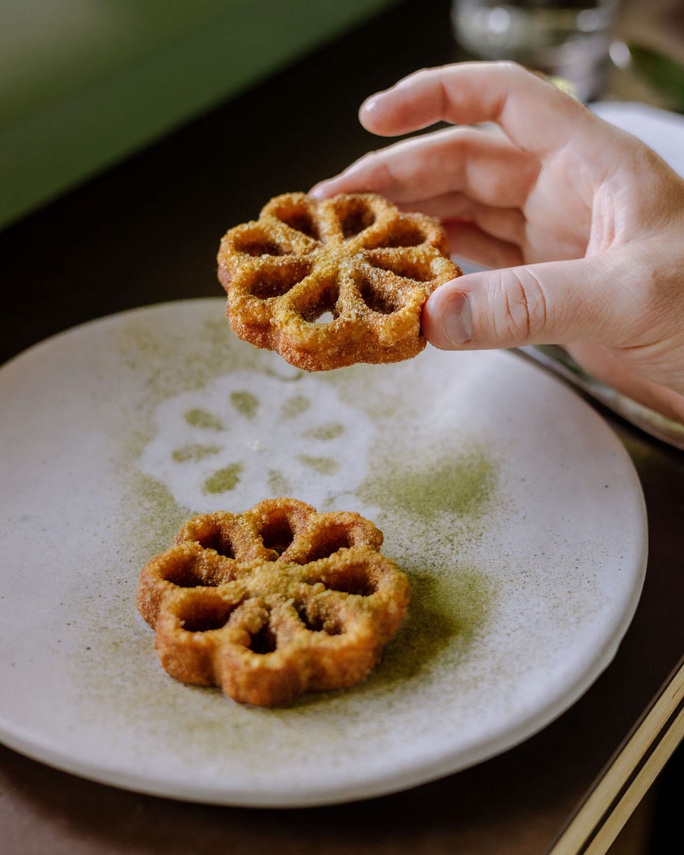 a hand holds a decorative dessert shaped like a flower with another similar piece on a plate