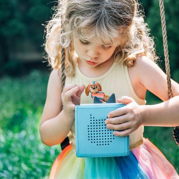 a girl sits on a swing holding her toniebox and paw patrol liberty tonie character, part of a good housekeeping review of the toniebox and tonies