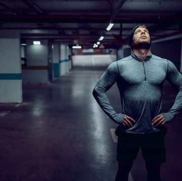 Attractive fit caucasian sportsman in active wear standing in garage with hands on hips and resting.