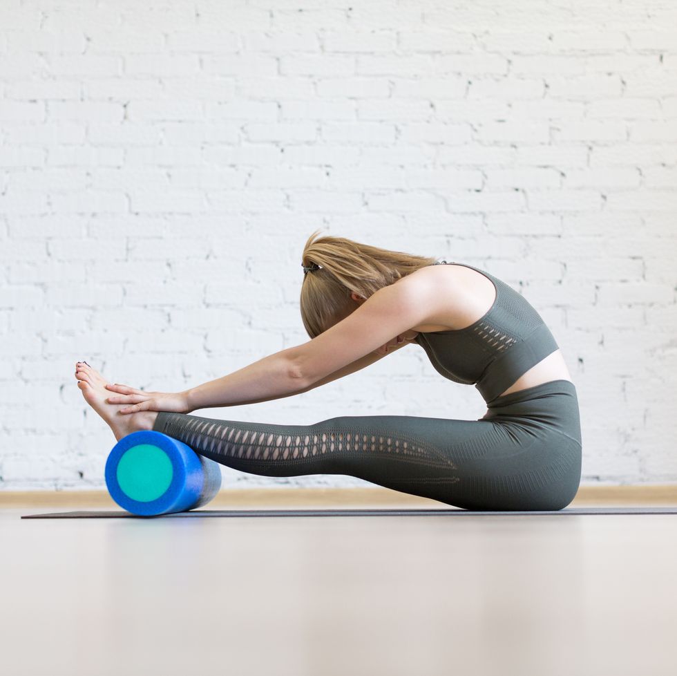attractive woman doing typical stretching, head to knees with foam blue roller, paschimottanasana pose, indoor at club