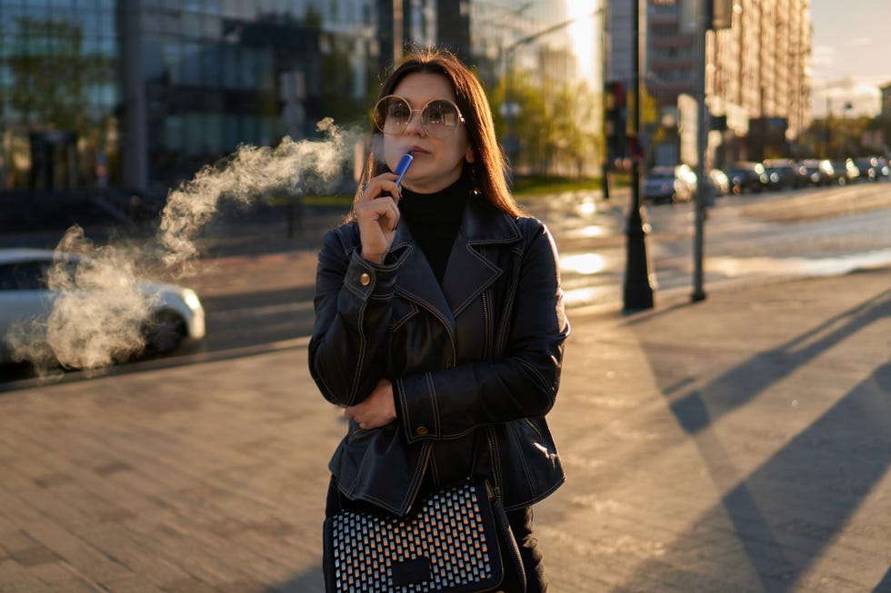 attractive young female smoking in the street lady of a millennial generation vaping a vaporizer fashion photography background with space for design