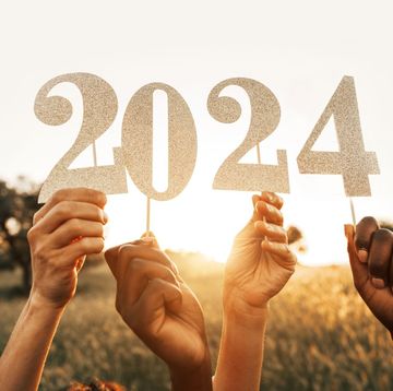 two pairs of hands holding up 2024 new year's sign against backdrop of rural field and sky