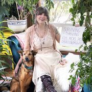 aunia kahn sitting in a white dress petting her dog, she carries a sign that says surviving and thriving with her invisible disabilities