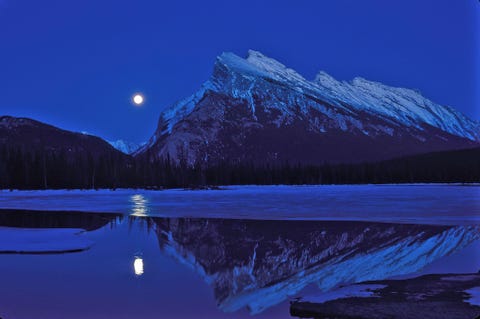 Een volle maan verschijnt boven Vermilion Lake naast Mount Rundle in Banff National Park Canada tijdens de herfst equinox