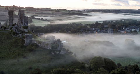 Een laaggelegen mist omringt het dorp Corfe Castle in Dorset Engeland terwijl de dageraad aanbreekt op de dag van de herfstnachtevening