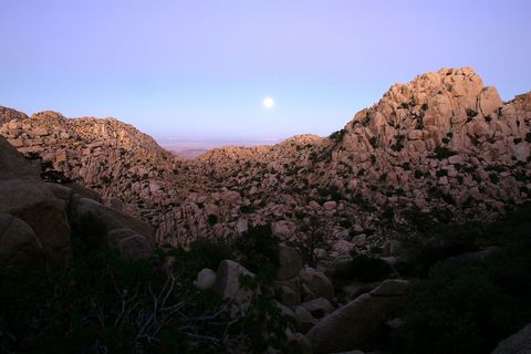 Een volle oogstmaan markeert de herfstnachtevening terwijl deze oprijst boven een woestijnachtig berglandschap gemaakt van enorme rotsformaties nabij Jacumba Californi