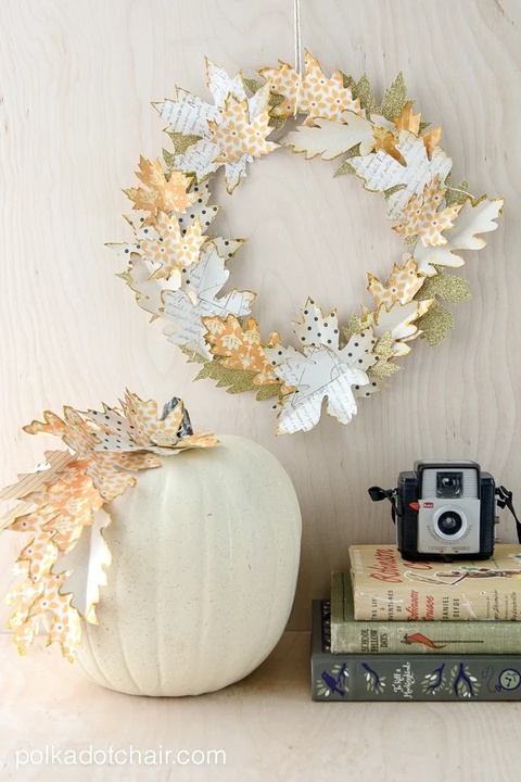 wreath made of leaves in different prints and patterns in fall colors hanging above a white pumpkin and stacked booked
