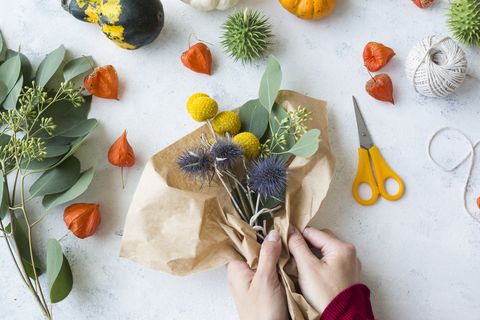 Autumnal decoration, ornamental pumpkins, hands wrapping bunch of flowers